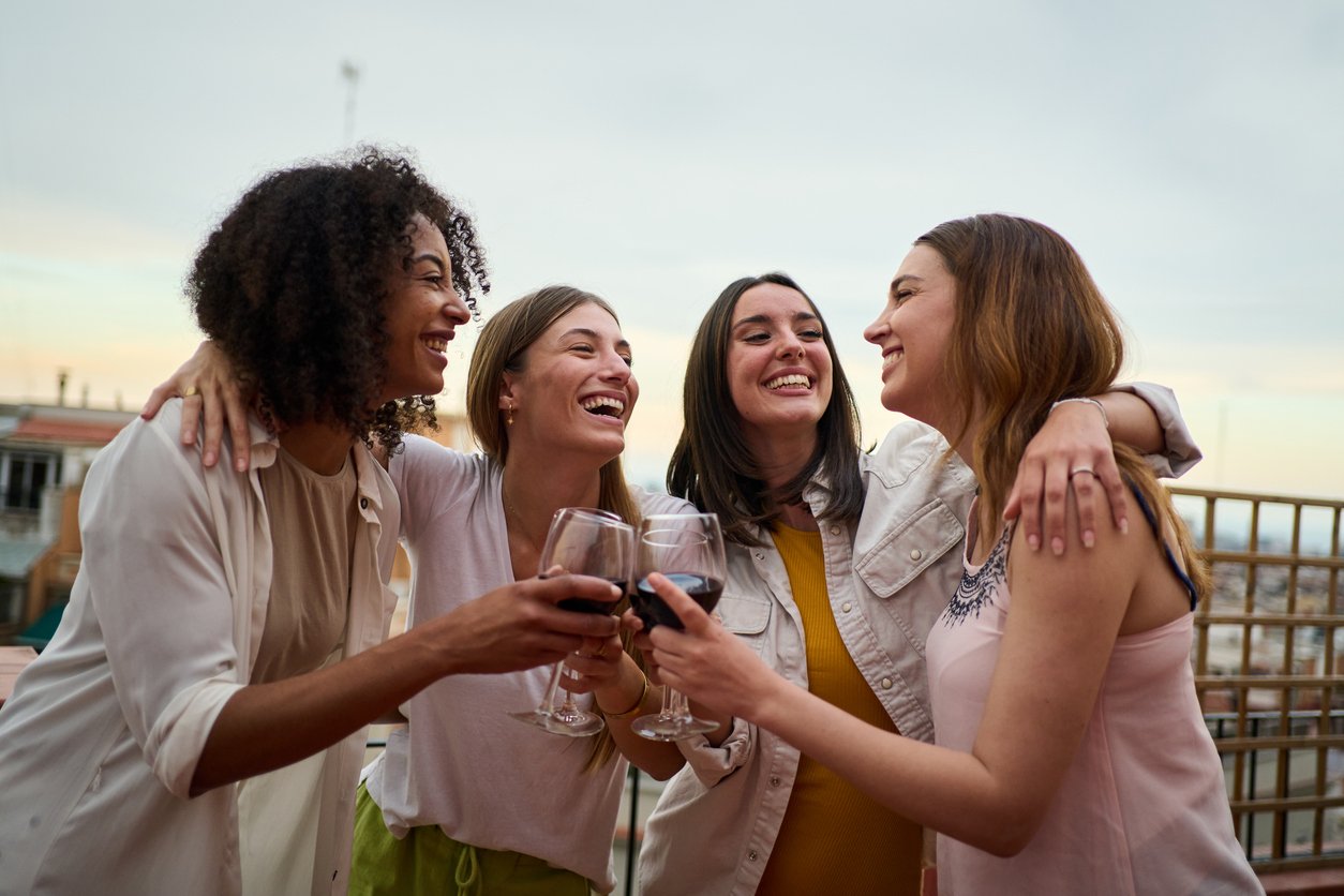Group multiracial smiling female friends toasting glasses red wine and celebrating party outdoors.